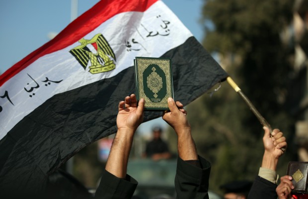 An Egyptian man holds up the a copy of Quran next to a national flag during a protest held by Muslim Salafi groups against the French military attack on Mali, in front of the French embassy in Giza, Egypt Friday, Jan. 18, 2013.   France launched airstrikes on Jan. 11, to help the government of Mali defeat al-Qaida-linked militants. (AP Photo/Khalil Hamra)