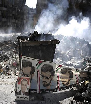 A banner portraying Basil, the late brother of Bashar al-Assad, and a poster of his late father Hafez, is seen near a burning pile of garbage in the Saif al-Dawlah neighborhood of Aleppo. (AFP)