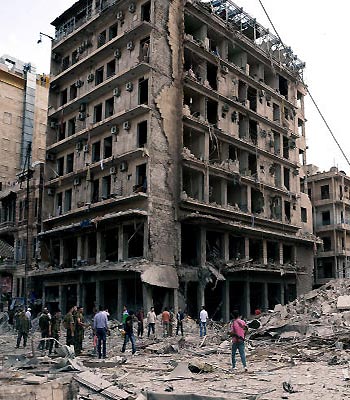 Syrian security officers gather at the scene in front of destroyed buildings where triple bombs exploded at the Saadallah al-Jabri square, in Aleppo city, Syria. (AP)