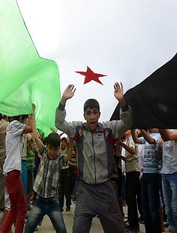Syrian boys gesture under a giant pre-Baath flag held by demonstrators during an anti-regime protest in the northern city of Aleppo on October 5, 2012. (AFP)