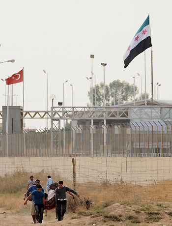 Syrians carry a rebel injured during fighting with the Syrian army in the Syrian town of Tel Abyad, background behind border gate, to the Turkish city of Akcakale on the Turkey-Syria border, Turkey, Friday, Oct. 5, 2012. (AP)
