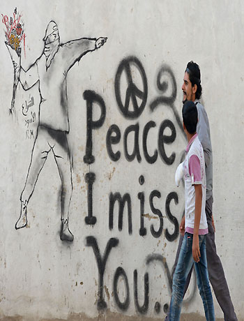 Syrian youths walk past graffiti in the rebel-held Syrian city of Minbej on October 10, 2012. (AFP)