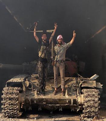 Two members of the Free Syrian Army stand on a tank as they gesture "V" for victory in the Saraqib area near the northern city of Idlib. (R)