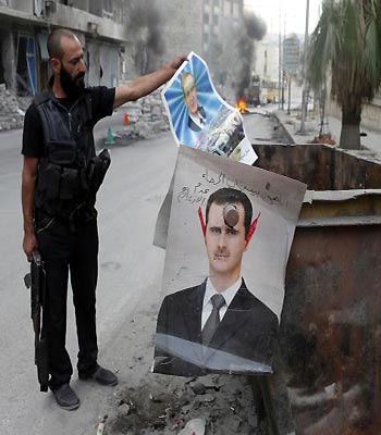 A member of the Free Syrian Army holds up a poster of Hafez al-Assad the father of Bashar al-Assad, whose defaced picture is seen hanging on a garbage bin in the city of Aleppo. (R)
