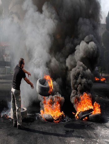 A protester throws a burning tire onto a pile of other tires used as a roadblock to protest the death of Brig. Gen. Wissam al-Hassan n a car bomb attack targeting his convoy, in the southern port city of Sidon, Lebanon, Saturday, Oct. 20, 2012. (AP)