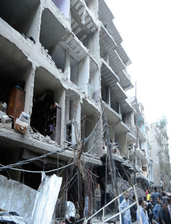 In this image released by the Syrian official news agency SANA , a crowd gather beneath the shattered facade of a building damaged by a car bomb in Damasus, Syria Friday Oct 26 2012. (AP)