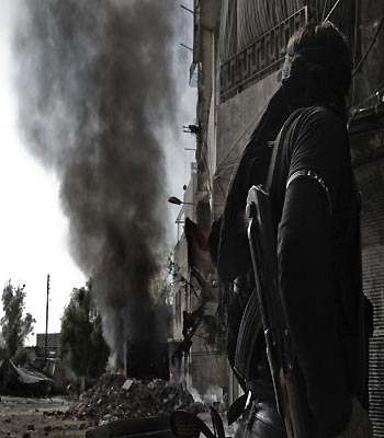 A Syrian rebel fighter looks at smoke billowing from a bus that caught on fire after a regime sniper allegedly shot at it in the northern city of Aleppo. (AFP)