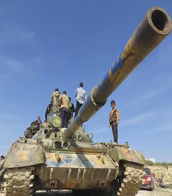 A boy stands next to Free Syrian Army fighters atop a tank after they defeated government troops at Salqin city near Idlib. (R)