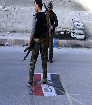 A member of the Free Syrian Army stands over a Syrian flag with the picture of Syria's President Bashar al-Assad at a checkpoint in Aleppo. (R)