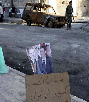 Members of the Free Syrian Army are seen behind images of Bashar al-Assad and his father Hafez at a checkpoint in Aleppo. The words read: "Bashar sold the Syrian People to Iran." (R)
