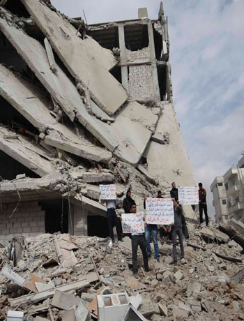 Demonstrators hold placards at damaged buildings during a protest against Syria's President Bashar al-Assad, after Friday prayers in Erbeen near Damascus. (Reuters)