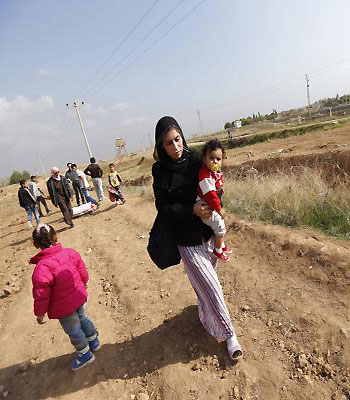 A Syrian refugee woman holding her daughter makes her way after crossing from northern Syrian town of Ras al-Ain to Turkey in the border town of Ceylanpinar, Sanliurfa province. (R)