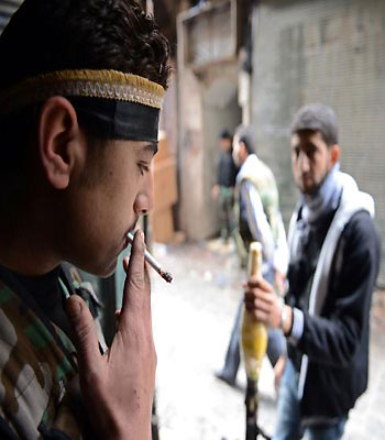 A Syrian rebel smokes a cigarette as his comrade stands guard with a Rocket Propelled Grenade (RPG) in a street in the old city of Aleppo, on November 12, 2012. (AFP)