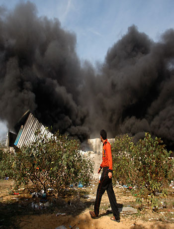 A Palestinian man walks past a fire after an Israeli airstrike on a wood factory in east Jabaliya, north Gaza, Friday, Nov. 16, 2012. (AP)