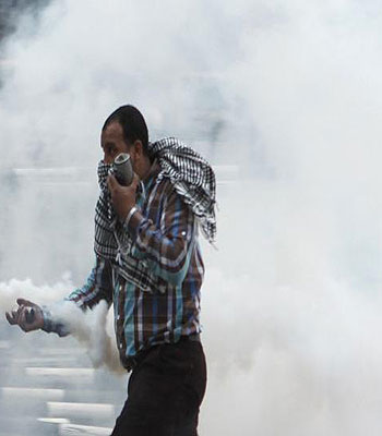 An anti-Mursi protester runs to throw a tear gas canister back at police during clashes in front of the Supreme Judicial Council in Cairo. (R)