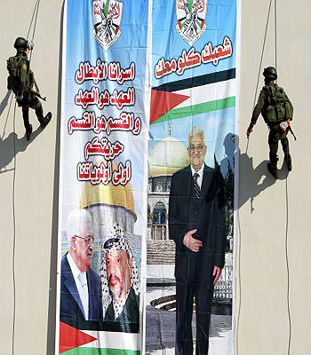 Palestinian security officers slide down from a building next to a banner of President Mahmoud Abbas with Yasser Arafat, in the West Bank town of Jenin, Wednesday, Nov. 28, 2012. (AP)