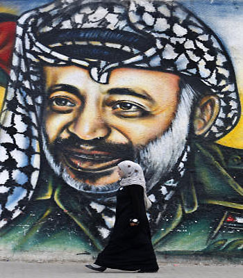 A Palestinian woman walks past a mural of late Palestinian leader Yasser Arafat, in Gaza City. (AP)