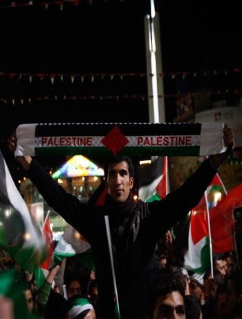 Palestinians wave Palestinian flags as they watch a large screen showing the U.N. General Assembly votes, In the west bank city of Ramallah, Thursday, Nov. 29, 2012. (AP)