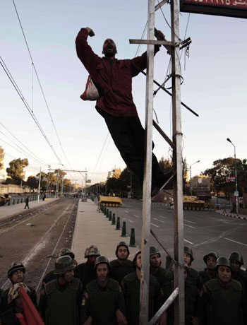 An Egyptian protester shouts slogans as he climbs on a pole in front of Egyptian soldiers standing guard near the presidential palace in Cairo on December 7, 2012. (AFP)