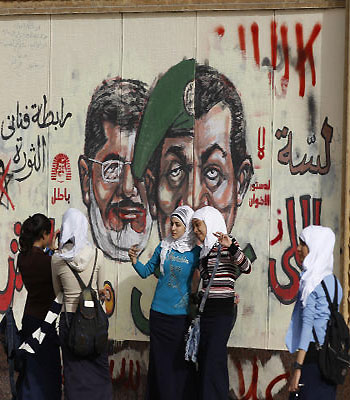 Young girls pose for a photograph by graffiti showing President Mursi, former Defense Minister Tantawi, and former President Mubarak, in Cairo, Egypt. (AP)