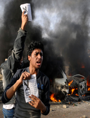 Opponents of Egyptian President Mohammed Morsi hold pamphlets urging a "no vote" on a constitutional referendum as cars burn during clashes between supporters and opponents of President Morsi in Alexandria, Egypt, Friday, Dec. 14, 2012. (AP)