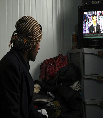 A Syrian refugee watches a television broadcast of Syria's President Assad speaking in Damascus, in their container at the Al-Zaatari refugee camp in Mafraq. (R)