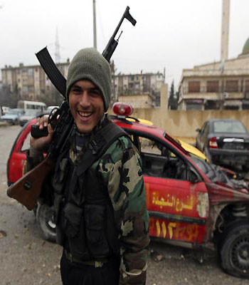 A Free Syrian Army fighter smiles as he poses with his weapon in front of a damaged car in Aleppo. (R)