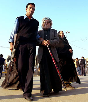An Iraqi policeman escorts an Iraqi elderly to a polling station to cast his vote in central Baghdad, 15 December 2005 (AFP)