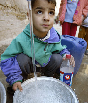 An Iraqi child fills a cooking pot with water from a stand pipe as Baghdad suffers from water shortages 28 December 2005 (AFP)