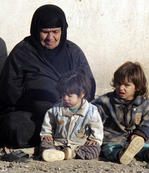 An Iraqi woman and children sit outside outside their house as they enjoy the sunshine in Baghdad December 29, 2005 (REUTERS)