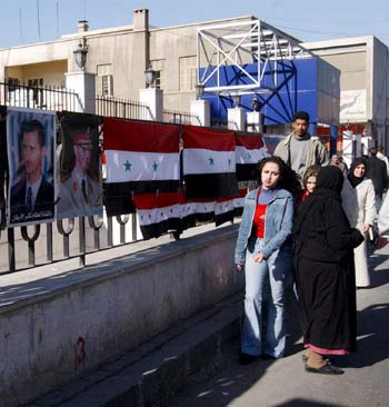 Local citizens pass new posters of Syrian President Bashar Assad in Damascus (EPA)
