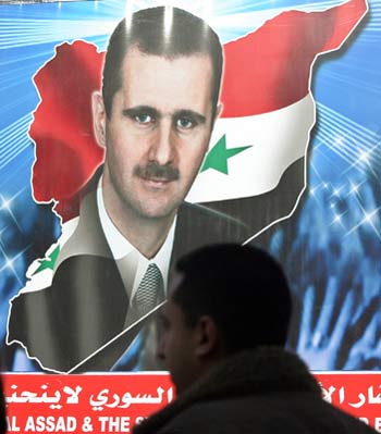 Syrians walks in front of picture of Syrian President al-Assad on street in Damascus (R)