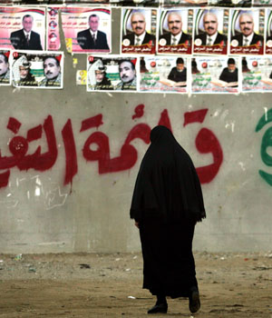 A veiled Palestinian woman walks by a wall painted with the symbol of the Islamic group Hamas next to the Akram School, which has been destroyed in an Israeli strike and rebuilt, in Gaza City, Jan 30, 2006 (AP)