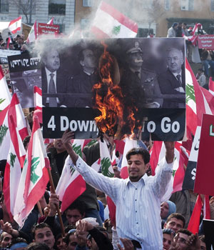 A Lebanese protester, surrounded by national flags, holds up a burning placard with portraits of Lebanese President Emile Lahoud and four pro-Syrian generals during demonstration held 14 February 2006 in downtown Beirut's Freedom Square (AFP)