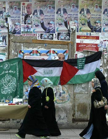 Palestinian girls walk past the green flags of the newly ruling Hamas party (AFP)