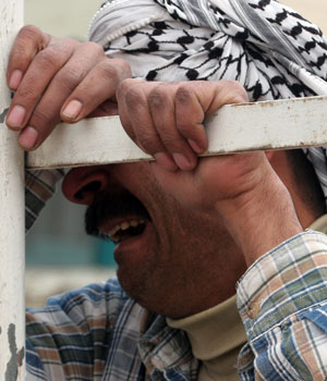 An Iraqi grieves while holding the bars of a truck that carries coffins during the funeral procession for victims of the previous days explosion in Baghdad, Feb. 22, 2006 (AP)