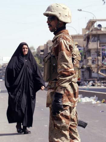An Iraqi woman walks near a soldier standing guard in Baghdad (R)