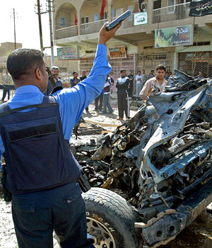 An Iraqi policeman brandishes his gun to disperse people at the site where a car bomb exploded in Baghdad's Zaafraniya district,07 March 2006 (AFP)