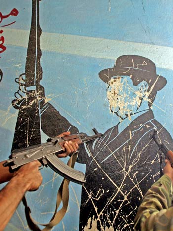 Iraqi soldiers point their guns gun on a defamed painting of ousted Iraqi dictator Saddam Hussein in the southern city of Basra (AFP)
