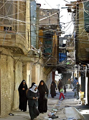 Iraqis walk through streets festooned with tangles of power lines coming from personal generators used to provide neighborhoods with electricity (AFP)