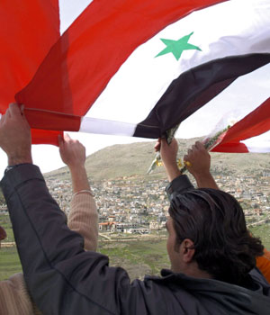 Syrian students wave national flags as they gather in the fields on the Syrian side of the Golan Heights to wish their mothers in the Israeli-occupied Druze village of Majdal Shams (background) a happy Mother's Day, 21 March 2006 (AFP)
