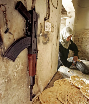 An Iraqi woman buys bread from a bakery shop where an assault rifle is seen hanging on one of its walls south of Baghdad, 03 April 2006 (AFP)