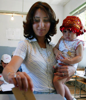 A Lebanese woman casts a vote as she holds her child (R)