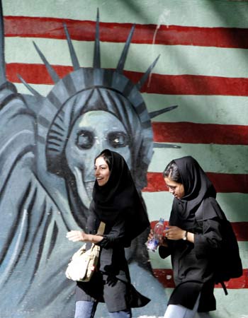 Iranian young women walk past a satirical mural of Statue of Liberty in Tehran (R)