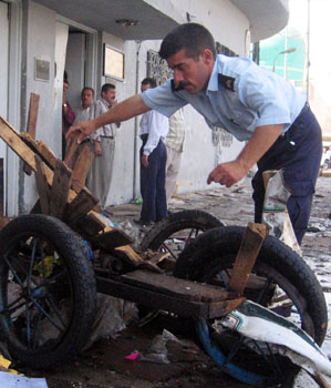 Iraqi policeman removes debris at the scene where a roadside bomb killed at least  18 people (AP)