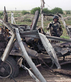 An Iraqi soldier stands guard near a mini-bus after a bomb attack along a road in Baquba, 65 km (40 miles) northeast of Baghdad May 10, 2006 (REUTERS)
