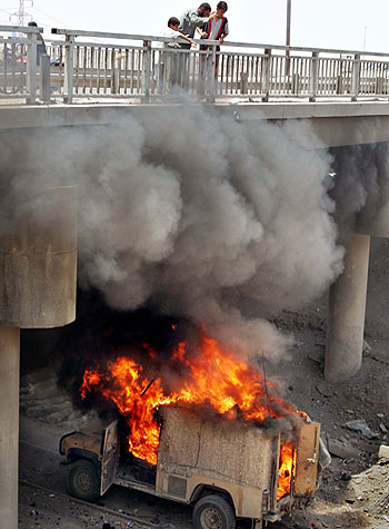 Three Iraqis standing on a bridge look down as one of them pours petrol onto a burning British military vehicle after a roadside bomb attack (AP)
