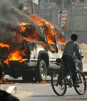 A boy cycles past a burning vehicle in Gaza City 25 May 2006, following clashes between Fatah and Hamas security members (AFP)