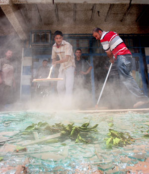 Shopkeepers sweep up broken glass after a controlled explosion by police detonated a roadside bomb in Palestine Street in eastern Baghdad, Iraq, May 27, 2006 (AP)