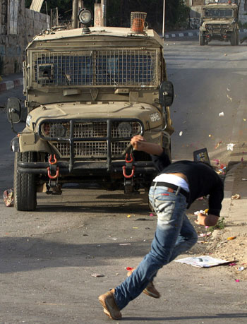 A Palestinian youth runs away from Israeli army jeeps during a military operation in the West Bank (AFP)